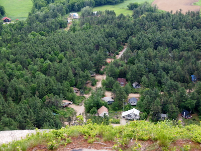 [Heavily treed landscape with a few homes and a road visible in the green blanket. In the foreground is the edge of the cliff.]